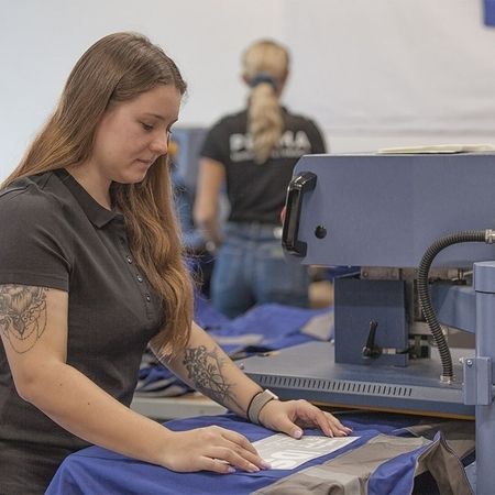 Arbeit im Patchraum: ein Frau bedient eine Maschine uns bedruckt ein Kleidungsstück