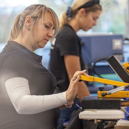 Arbeit im Patchraum: ein Frau bedient eine Maschine uns bedruckt ein Kleidungsstück