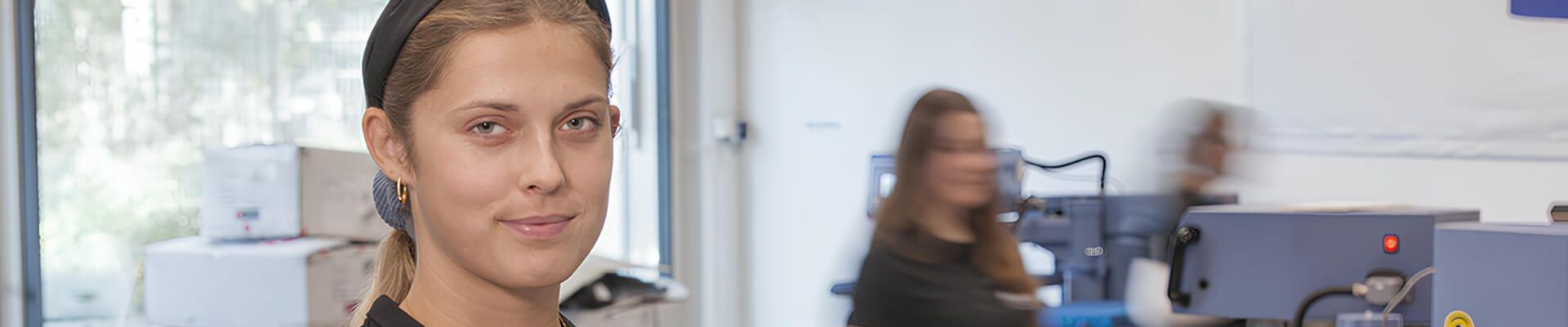 Een werknemer van Perma GmbH kijkt in de camera terwijl er op de achtergrond wordt gewerkt