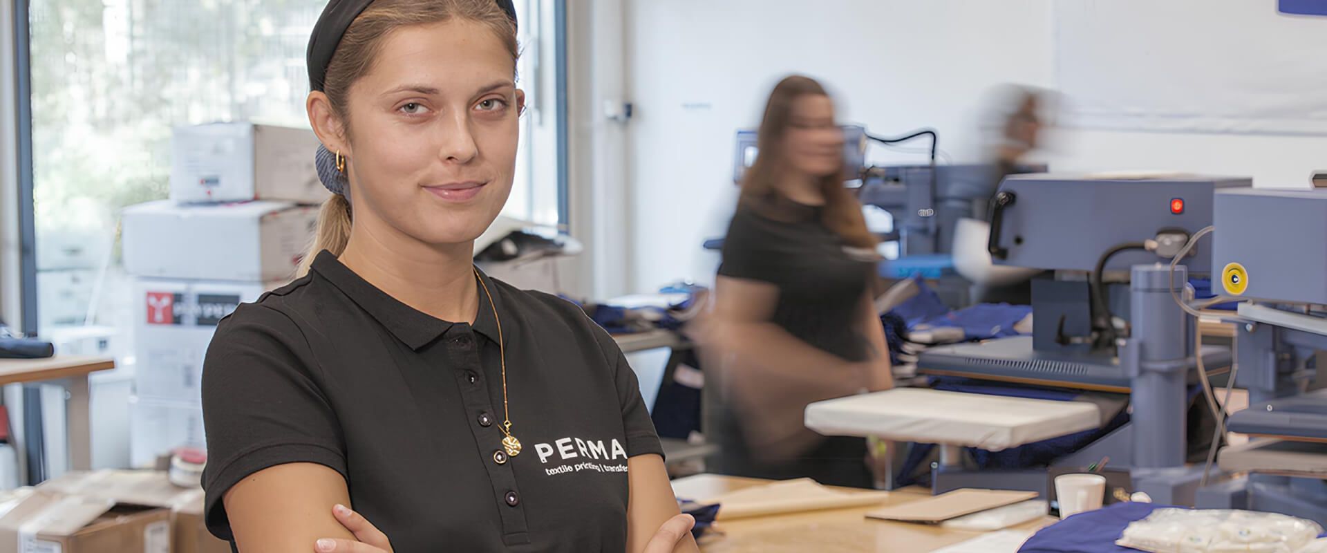 An employee of Perma GmbH looks into the camera while work is going on in the background.